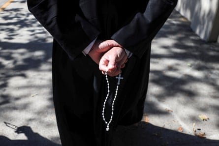 The hands of a Catholic priest in black seen from behind fingering a rosary 