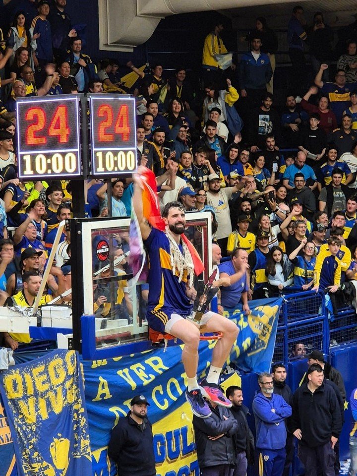 Sebastián Vega, con la bandera de la comunidad LGBT+ colgado del aro después de consagrarse bicampeón de la Liga Nacional con Boca.