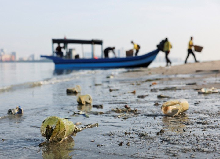 Vasos de plástico y otros objetos varados en una playa mientras voluntarios desembarcan de un barco durante una campaña de limpieza de playas organizada con motivo de la celebración del Día de la Tierra en George Town, Malasia, 22 de abril de 2024. REUTERS/Hasnoor Hussain